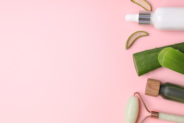 Cosmetic products, cut aloe leaves and face roller on pink background, flat lay. Space for text