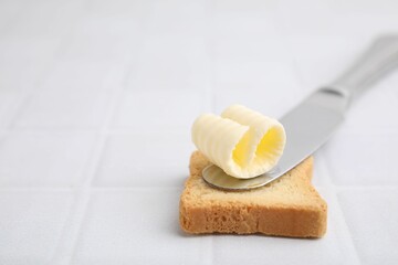Tasty butter curl, knife and piece of dry bread on white tiled table, closeup. Space for text