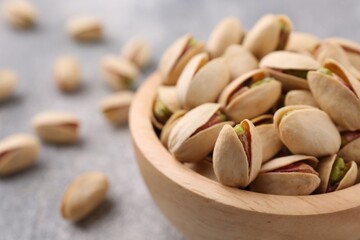 Delicious pistachios in bowl on grey textured table, closeup