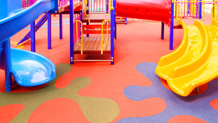 Colorful slides with playground climbing equipment on rubber floor in outdoors playground area at...