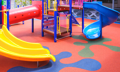 Colorful slides with playground climbing equipment on rubber floor in outdoors playground area at kindergarten
