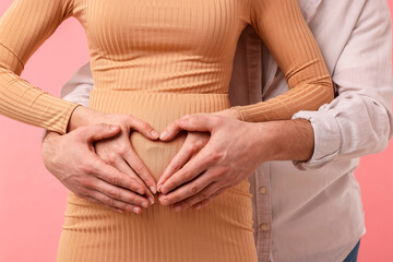Pregnant woman and her husband making heart with hands on belly against pink background, closeup