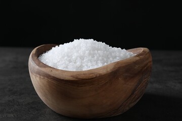 Natural salt in wooden bowl on dark grey table, closeup