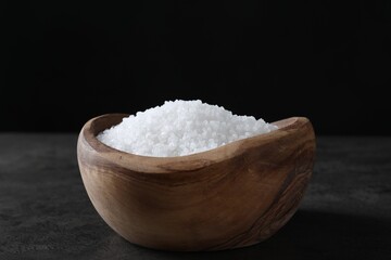 Fototapeta na wymiar Natural salt in wooden bowl on dark grey table, closeup