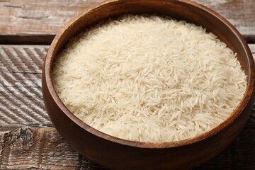 Raw basmati rice in bowl on wooden table, closeup