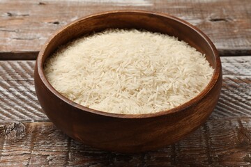 Raw basmati rice in bowl on wooden table, closeup