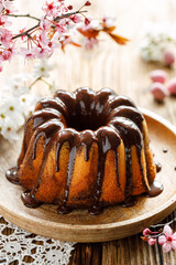 Chocolate and vanilla marble bundt cake, Babka with chocolate glaze on a plate on a wooden table decorated with spring flowers. Delicious easter dessert
