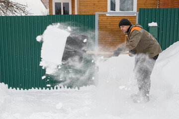 A man in work clothes removes snow near his house.