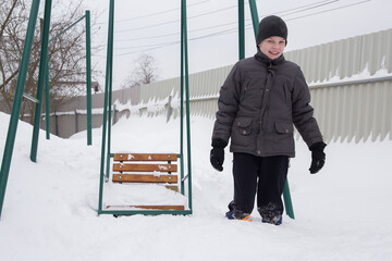 A boy stands in deep snow next to a snow-covered swing.