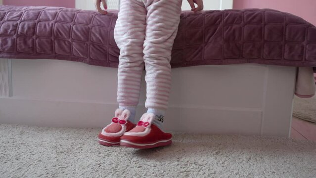 little girl puts on bunny slippers, a child gets out of bed and puts on slippers, a girl in winter slippers