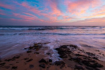 Colorful clouds over the beach shore at sunrise time.