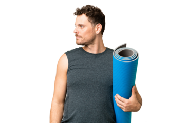 Young sport man going to yoga classes while holding a mat over isolated chroma key background looking to the side