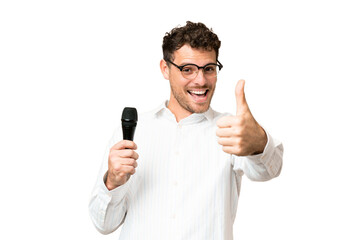 Brazilian man picking up a microphone over isolated chroma key background with thumbs up because something good has happened