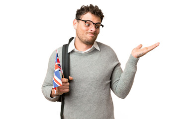 Brazilian man holding an United Kingdom flag over isolated chroma key background having doubts while raising hands