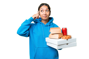 Young Uruguayan woman holding pizzas and burgers over isolated chroma key background having doubts...