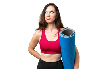 Young sport woman going to yoga classes while holding a mat over isolated background and looking up