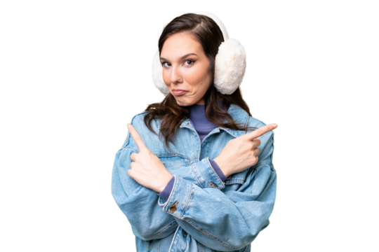 Young caucasian woman wearing winter muffs over isolated background pointing to the laterals having doubts