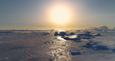 Fly over polar frozen ocean landscape in sunset. Serene beauty of glaciers surrounded by pristine icy snow land. Untouched wilderness of Antarctica. South Pole travel background. Low angle drone shot