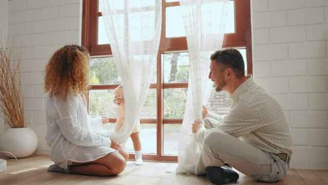 Cheerful parents playing with daughter together in living room at home. Father and mother take care give time to little baby in bedroom at house. Family relationship concept.