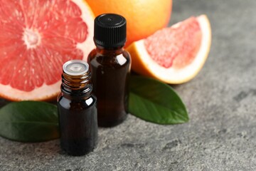 Grapefruit essential oil in bottles, leaves and fruits on dark textured table, closeup. Space for text