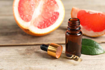 Grapefruit essential oil in bottle, pipette, leaf and fruit on wooden table, closeup. Space for text