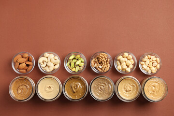 Many tasty nut butters in jars and nuts on brown table, flat lay. Space for text