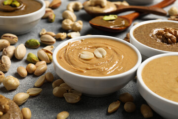 Tasty nut butters in bowls and raw nuts on light grey table, closeup