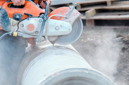 Construction worker cutting concrete pipe for drainage using a cut-off saw. Cutting concrete with a diamond blade creating cloud of silica dust
