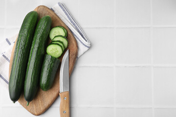 Fresh cucumbers and knife on white tiled table, top view. Space for text