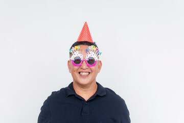 Middle-aged Asian man with a big smile celebrating his birthday in a party hat and novelty glasses...