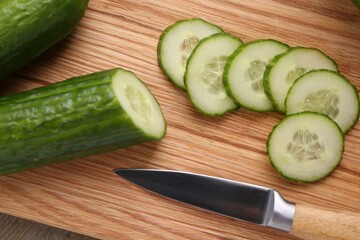 Cut cucumber and knife on wooden board, top view
