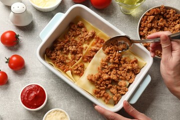 Woman making lasagna at light grey textured table, top view