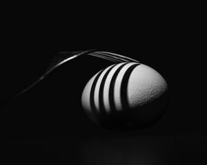 Abstract black and white dark still life image of brightly lit egg and fork with contrasting shadows