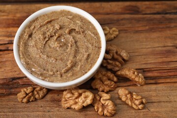 Delicious nut butter in bowl and walnuts on wooden table, closeup