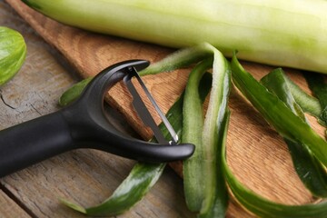 Fresh cucumber, peels and peeler on wooden table, closeup