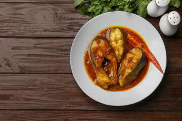 Tasty fish curry served on wooden table, flat lay. Space for text. Indian cuisine