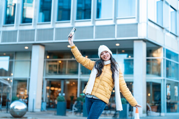 smiling young woman having fun time, using mobile phones outdoor in an urban winter city. people, communication, shopping and lifestyle concept