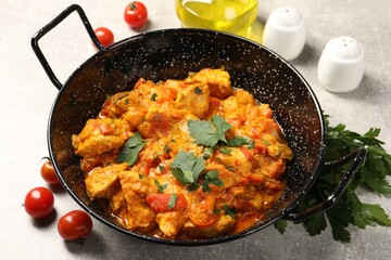 Delicious chicken curry in frying pan, parsley and tomatoes on light grey table, closeup