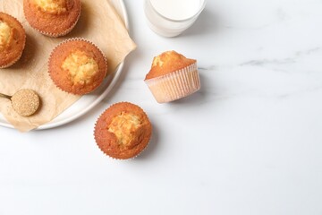 Delicious sweet muffins, glass of milk and brown sugar on white marble table, flat lay. Space for text
