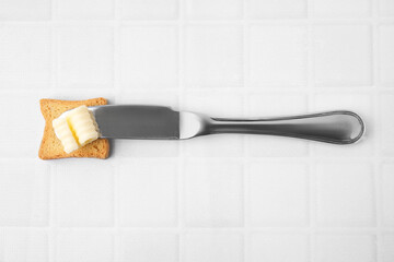 Tasty butter curl, knife and piece of dry bread on white tiled table, top view