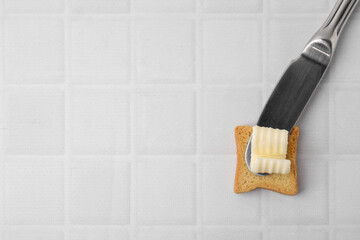 Tasty butter curl, knife and piece of dry bread on white tiled table, top view. Space for text