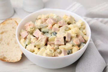 Tasty Olivier salad with boiled sausage in bowl and bread on white table, closeup