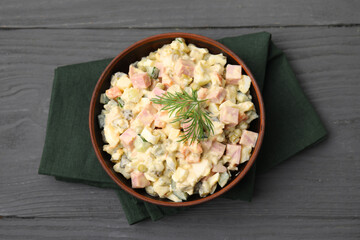 Tasty Olivier salad with boiled sausage in bowl on grey wooden table, top view