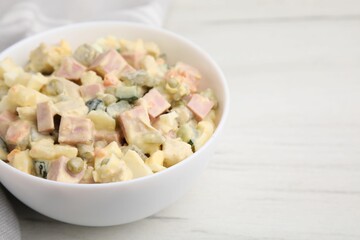 Tasty Olivier salad with boiled sausage in bowl on white table, closeup. Space for text