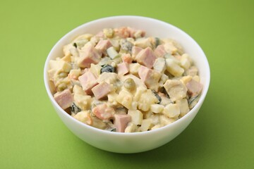 Tasty Olivier salad with boiled sausage in bowl on green table