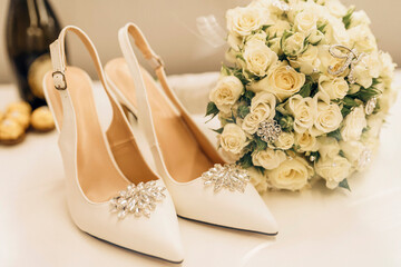 Beautiful bridal fashionable wedding white high heels shoes,  and a bridal bouquet on a desk at home.  Wedding
