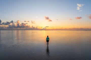  A female traveler standing on be beach in sunrise with reflection background