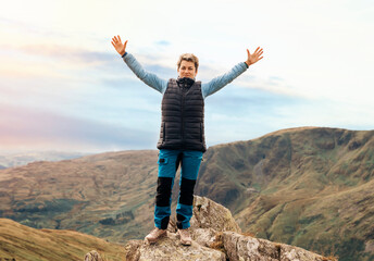 Woman reaching the destination and on the top of mountain against cloudy blue sky on autumn day Travel Lifestyle concept The national park Lake District in England - obrazy, fototapety, plakaty