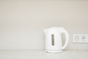 New white plastic electric kettle with plug in wall outlet socket on stone table top at home...