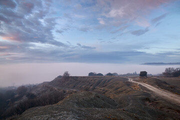 Sunrise on top of a mountain with a dirt road the silhouettes of vegetation a sky covered in blue and red clouds